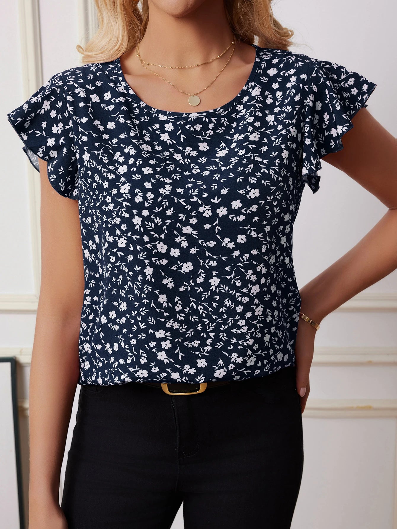 Woman wearing navy blue boho floral chiffon blouse with white flower pattern and flutter sleeves, styled with black jeans for casual chic look.